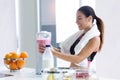 Sporty young woman preparing strawberry and banana smoothie with blender in the kitchen at home