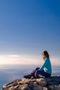 Sporty young woman sitting in a rocky top of the mountain against the blue of sky and sea Royalty Free Stock Photo