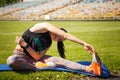 Sporty young woman stratching muscles on yoga mat on stadium green lawn. Sport physical training, healthy way of life, flexibility Royalty Free Stock Photo