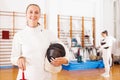 Sporty young woman in uniform standing at fencing workout