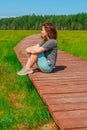 A sporty young woman walks along a picturesque wooden walking path through a swamp with tall grass in summer. Royalty Free Stock Photo