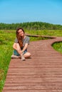 A sporty young woman walks along a picturesque wooden walking path through a swamp with tall grass in summer. Royalty Free Stock Photo