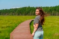 A sporty young woman walks along a picturesque wooden walking path through a swamp with tall grass in summer. Royalty Free Stock Photo
