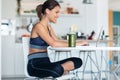 Sporty young woman working with her laptop after session of exercises in the kitchen at home