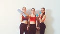 Sporty young women standing against wall. Sports background. Three fitness girls in gym after workout. Copy space. Females in spor Royalty Free Stock Photo