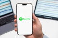 Spotify logo on the screen of smartphone in mans hand on the workplace background