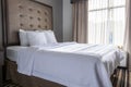 A spotless clean queen size hotel bed by a window in a bright hotel room.