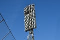 Spotlights in stadium against blue summer sky. High metal lighting tower for sports arena or stadium. Bottom up view.