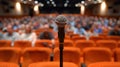 Spotlit microphone on stand in audience filled auditorium, setting for live performance.