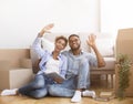 Spouses Using Tablet Sitting Among Moving Boxes Discussing Renovation Indoor