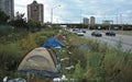 A sprawling makeshift encampment has taken root along the highway, surrounded by the imposing high-rise buildings of the