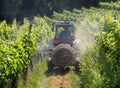 A sprayer machine, trailed by tractor, sprinkles pesticides among the rows of vineyards in summer .