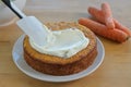 Spreading frosting on a freshly baked carrot cake, wooden table