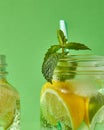 A sprig of green mint in focus in a glass jar with a refreshing natural handmade cocktail. Citrus fruits slices of lemon