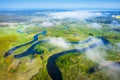 Spring aerial nature background. River landscape from above. Drone view of curved river on green meadow through white clouds on