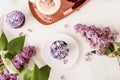 Spring aesthetic table setting. Purple french cupcakes on the golden tray, coffee cup and lilac flowers flat lay.