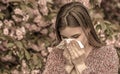 Spring allergy concept. Sneezing young girl with nose wiper among blooming trees in park. Pollen allergy, girl sneezing Royalty Free Stock Photo
