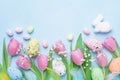 Spring background with flowers, bunny, colorful eggs and feathers on blue table top view. Happy Easter card.