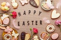 Spring background with text Happy Easter. Aesthetic pastel spring Easter cookies, pink flowers and eggs flat lay.