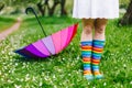 Girl`s legs in colorful rain boots with rainbow-umbrella on the background. Spring, outdoors.