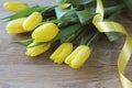 Spring bouguet of yellow tulips with green leaves and satin yellow ribbon close-up on wooden brown background.