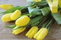 Spring bouguet of yellow tulips with green leaves and satin yellow ribbon close-up on wooden brown background.