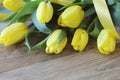 Spring bouguet of yellow tulips with green leaves and satin yellow ribbon close-up on wooden brown background.