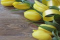 Spring bouguet of yellow tulips with green leaves and satin yellow ribbon close-up on wooden brown background.