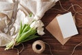 Spring bouquet of white tulip flowers, kraft envelope with blank card, scissors, twine on rustic wooden table. Wedding day composi Royalty Free Stock Photo