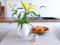 Spring breakfast still life with a cup of coffee and a wooden bowl with oranges. Lily flowers in a vase on a wooden