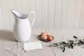 Spring breakfast still life scene. White jug, olive branch, chicken eggs on linen tablecloth. Blank greeting card mockup