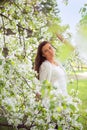 Spring brunette girl standing outdoor in blooming trees. Beautiful romantic woman in apple flowers. Young woman enjoying nature.