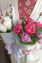 Spring buquets of white, pink and purple tulips, wrapped in white paper with fabric bows. In woman hands. Flower gift.