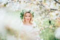 Spring coming! Beautiful young cheerful pregnant woman in wreath flowers on head touching belly while walking in spring tree garde Royalty Free Stock Photo