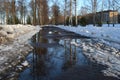 Spring is coming the month of March. Alley in the park with melting snow puddles and ice on a sunny spring day