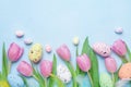 Spring composition with pink tulip, colorful eggs and feathers on blue table top view. Happy Easter card. Royalty Free Stock Photo