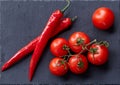 Composition of tomato bunch and hot pepper on black piece of board, top view, close-up. Royalty Free Stock Photo