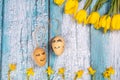 Spring composition of yellow flowers and eggs with a painted cute face on a blue background. Congratulations on Easter.