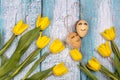 Spring composition of yellow flowers and eggs with a painted cute face on a blue background. Congratulations on Easter.