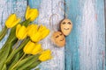 Spring composition of yellow flowers and eggs with a painted cute face on a blue background. Congratulations on Easter.