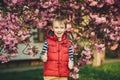 Spring day. Fashionable kid in spring park. Spring pink sakura blossom. Cute little stylish boy in the city. Kids fashion and