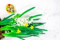 Spring, Easter concept. Yellow Easter eggs in a nest next to a bouquet of daffodils on a white concrete table. Place for