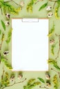 Spring easter floral frame and white blank paper. Natural tree branches, yellow flowers, quail eggs, clipboard notepad on green Royalty Free Stock Photo