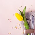 Spring Easter table setting. Cutlery is decorated with beautiful yellow tulip on pastel pink background Royalty Free Stock Photo