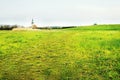 Spring evening photo flowering meadow with church and tower building over the horizon in czech nature during windy weather