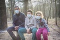 In the spring a father with children sits on a bench in the forest. Everyone has masks on their faces