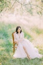 Spring field composition of the woman in the long white dress sitting in the old modern chair.