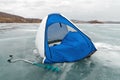 A fishing tent stands in the wind on the melting ice of the Big Lake against the shore. Krasnoyarsk region. Russia