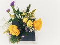 Spring floral arrangement in purple and yellow with roses and other flower blooms sitting on a black and white board with a white