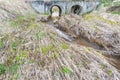 Spring flow of water in the bed of a small river passes through the large drainage pipes under the bulk bridge Royalty Free Stock Photo